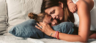 A young child laying with a woman on a bed